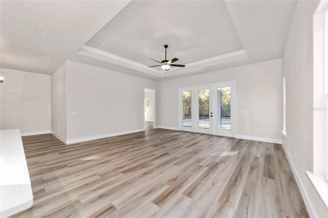 unfurnished living room featuring french doors, a tray ceiling, light hardwood / wood-style flooring, and ceiling fan