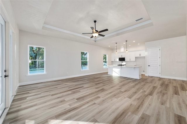 unfurnished living room with a tray ceiling, ceiling fan, and light hardwood / wood-style floors