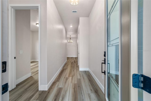 hall with light hardwood / wood-style flooring and an inviting chandelier