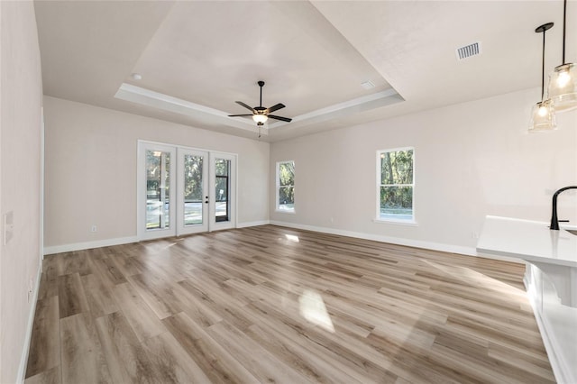 unfurnished living room featuring ceiling fan, light wood-type flooring, french doors, and a tray ceiling