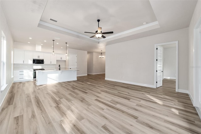 unfurnished living room featuring a raised ceiling, sink, ceiling fan with notable chandelier, and light wood-type flooring