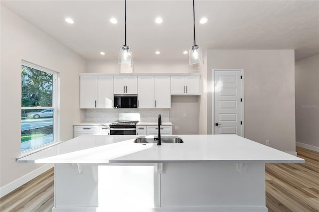 kitchen with white cabinetry, sink, stainless steel range oven, a large island with sink, and pendant lighting