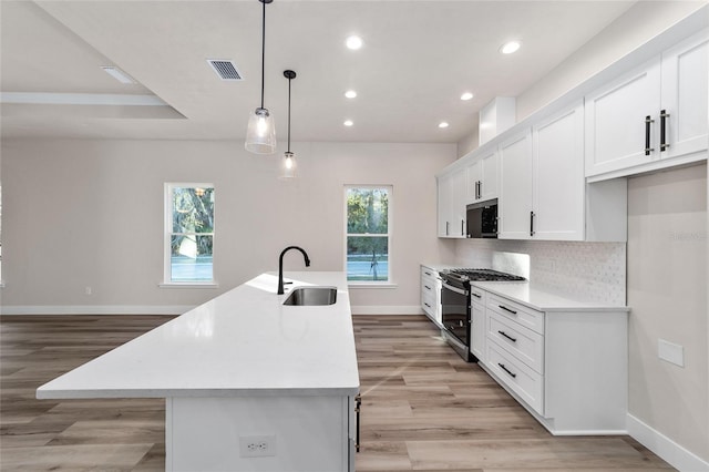 kitchen with a kitchen island with sink, sink, decorative light fixtures, and appliances with stainless steel finishes