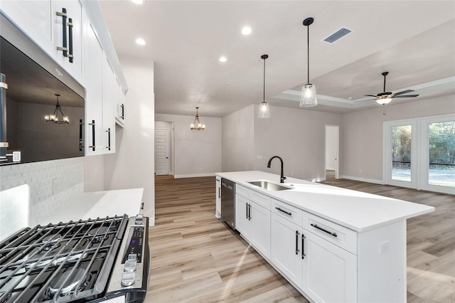 kitchen with white cabinets, ceiling fan with notable chandelier, sink, dishwasher, and an island with sink