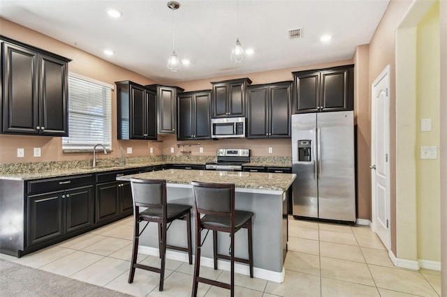 kitchen featuring light stone countertops, a center island, hanging light fixtures, light tile patterned flooring, and appliances with stainless steel finishes