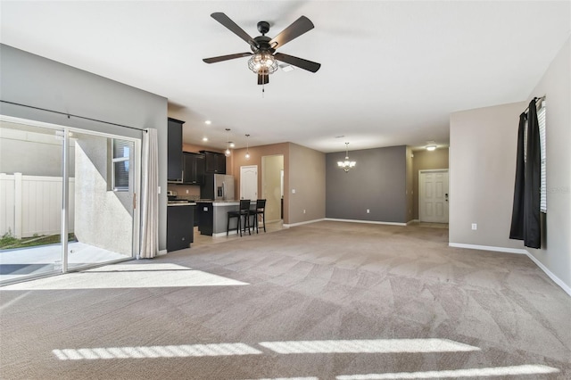 unfurnished living room with ceiling fan with notable chandelier and light colored carpet