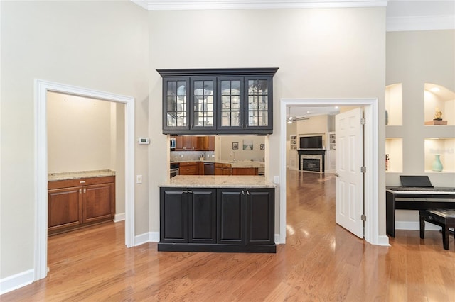 bar featuring ceiling fan, light hardwood / wood-style floors, light stone counters, and crown molding