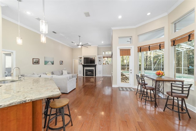 kitchen with sink, hanging light fixtures, crown molding, ceiling fan, and light stone counters