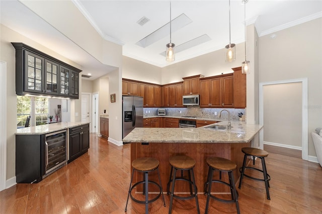 kitchen with a kitchen breakfast bar, sink, appliances with stainless steel finishes, kitchen peninsula, and beverage cooler