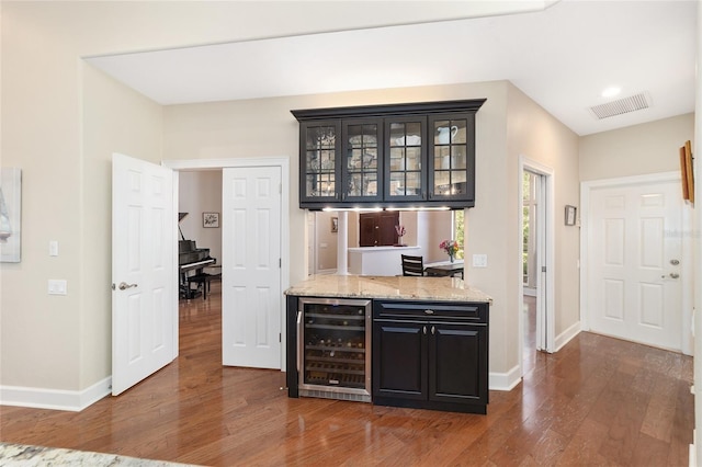 bar with light stone countertops, dark wood-type flooring, and beverage cooler