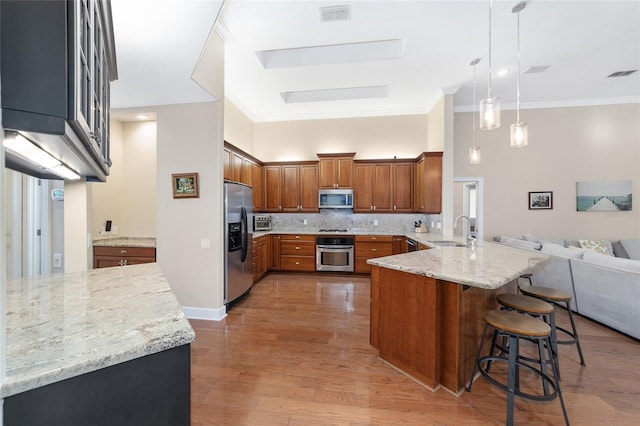 kitchen featuring sink, appliances with stainless steel finishes, light stone counters, kitchen peninsula, and a breakfast bar area