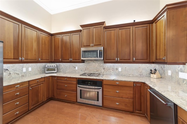 kitchen featuring decorative backsplash, light wood-type flooring, light stone countertops, ornamental molding, and appliances with stainless steel finishes