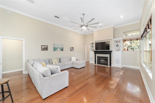 living room with hardwood / wood-style floors, a stone fireplace, ceiling fan, and ornamental molding