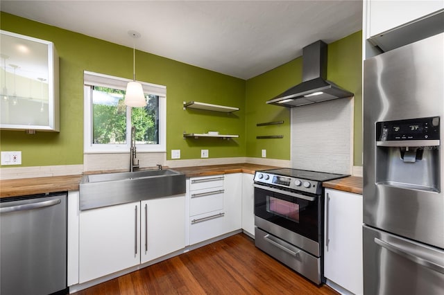 kitchen featuring sink, wall chimney exhaust hood, decorative light fixtures, white cabinetry, and stainless steel appliances