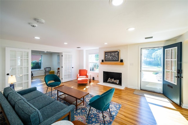 living room with plenty of natural light, a fireplace, light hardwood / wood-style floors, and french doors