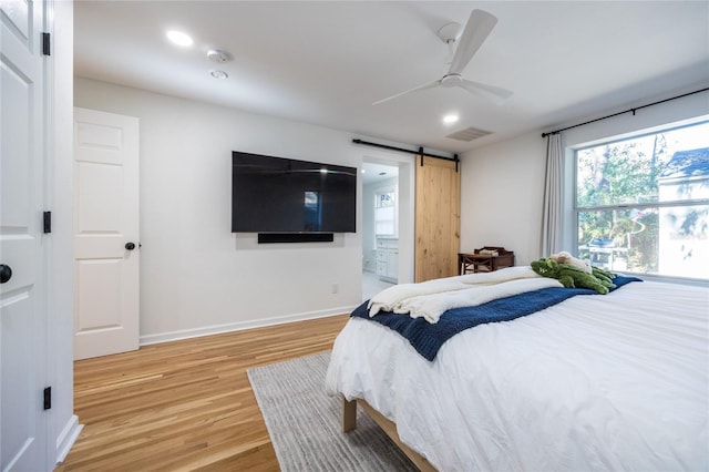 bedroom with ceiling fan, a barn door, wood-type flooring, and connected bathroom