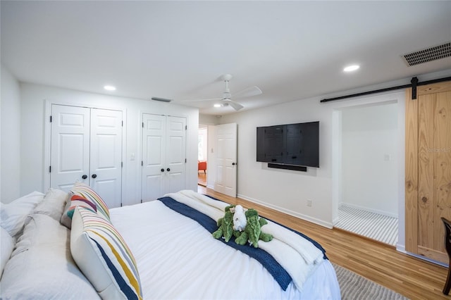 bedroom featuring hardwood / wood-style floors, a barn door, two closets, and ceiling fan