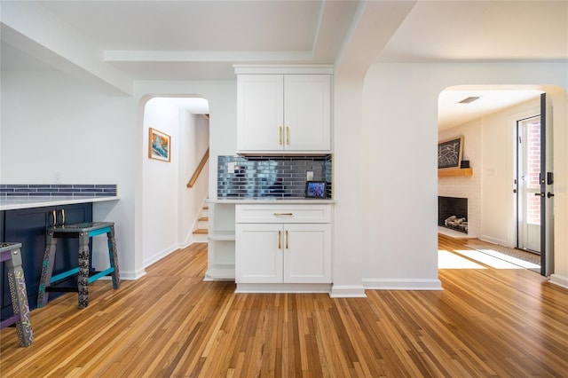 kitchen featuring backsplash, a fireplace, white cabinetry, and light hardwood / wood-style flooring