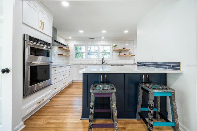 kitchen with white cabinets, a kitchen breakfast bar, kitchen peninsula, tasteful backsplash, and stainless steel double oven