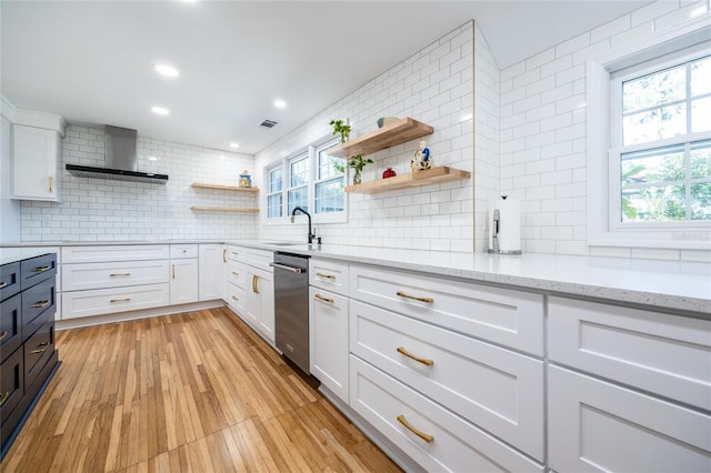 kitchen with light stone countertops, wall chimney range hood, light hardwood / wood-style flooring, backsplash, and white cabinets