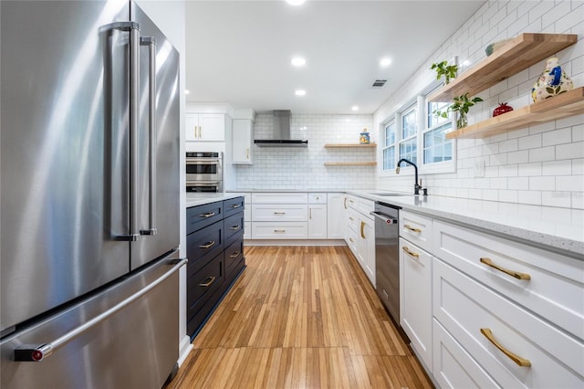 kitchen featuring light stone countertops, appliances with stainless steel finishes, sink, wall chimney range hood, and white cabinets