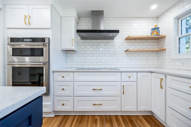 kitchen with wall chimney exhaust hood, light stone counters, double oven, black electric cooktop, and white cabinets