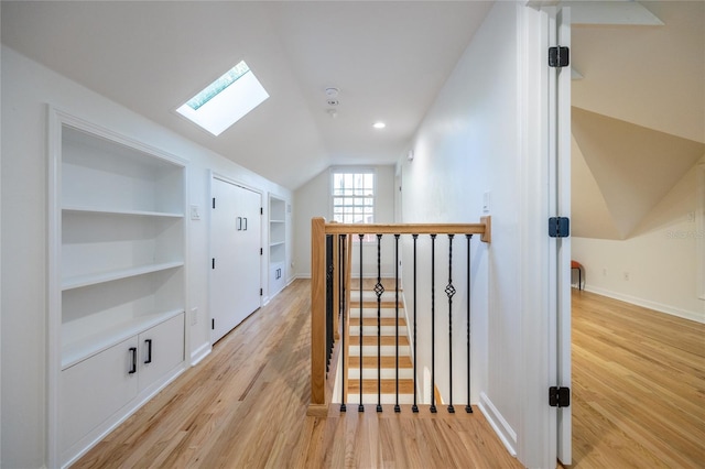 hallway featuring built in shelves, lofted ceiling with skylight, and light hardwood / wood-style floors