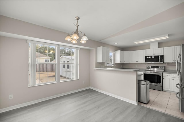 kitchen with lofted ceiling, hanging light fixtures, appliances with stainless steel finishes, white cabinetry, and a chandelier