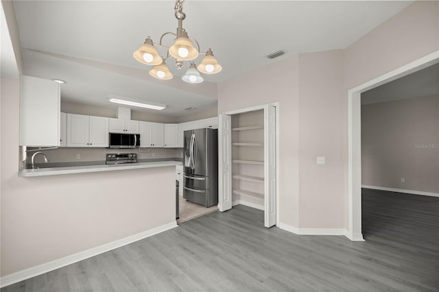 kitchen with stainless steel appliances, kitchen peninsula, pendant lighting, white cabinets, and light wood-type flooring