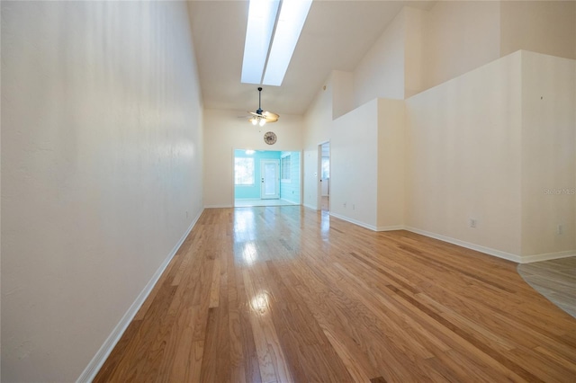 unfurnished living room with light wood-type flooring, a skylight, and high vaulted ceiling