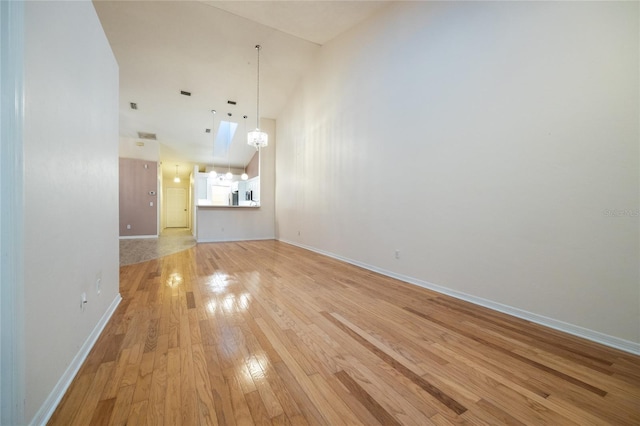 unfurnished living room featuring light wood-type flooring, high vaulted ceiling, and an inviting chandelier