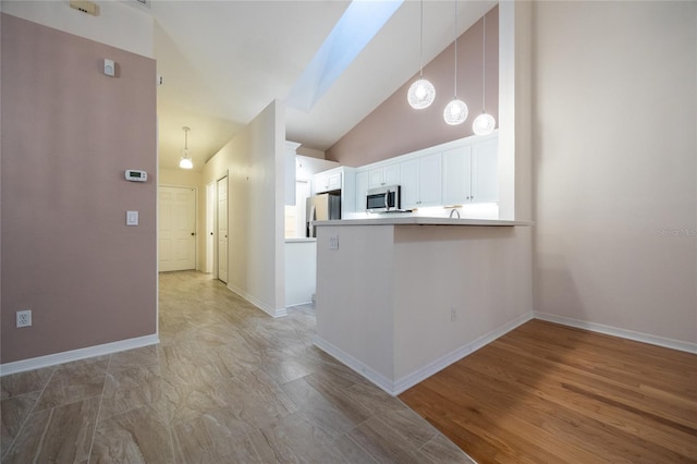 kitchen featuring kitchen peninsula, lofted ceiling, decorative light fixtures, white cabinets, and appliances with stainless steel finishes