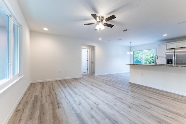 unfurnished living room with sink, light hardwood / wood-style floors, and ceiling fan with notable chandelier