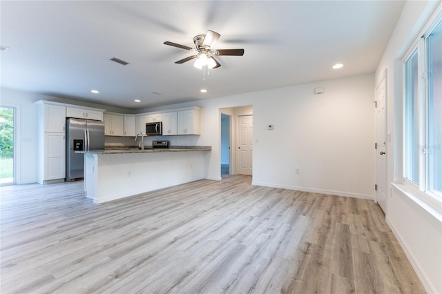 kitchen with appliances with stainless steel finishes, white cabinets, light hardwood / wood-style flooring, ceiling fan, and stone countertops