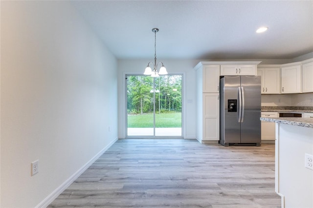 kitchen with stainless steel refrigerator with ice dispenser, pendant lighting, light wood-type flooring, white cabinets, and an inviting chandelier