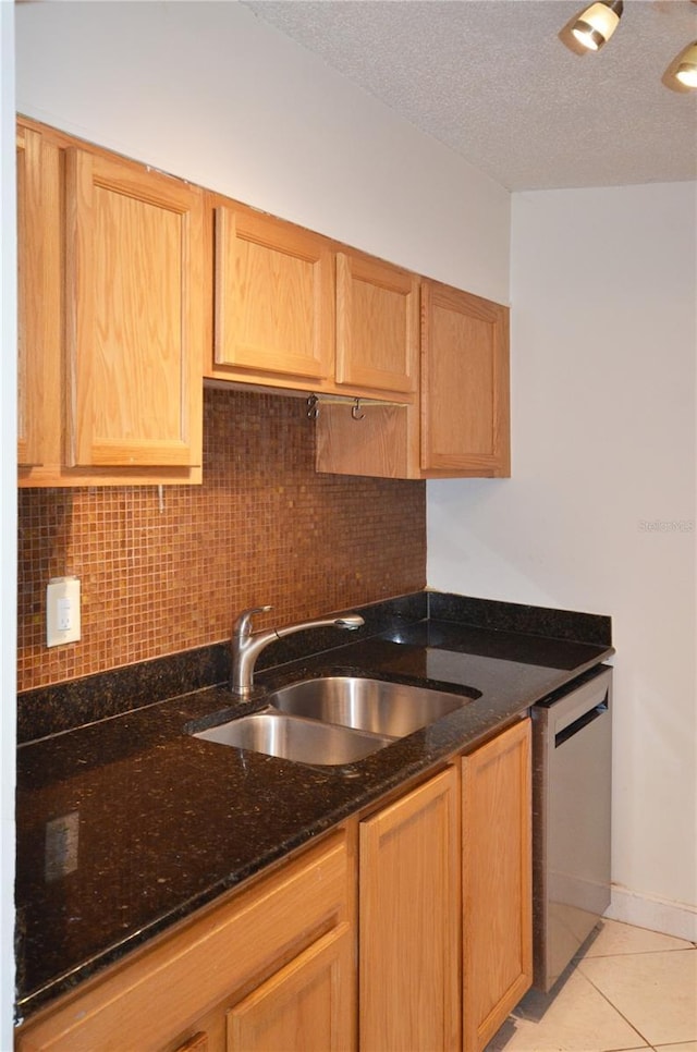 kitchen with dishwasher, sink, dark stone countertops, a textured ceiling, and light tile patterned flooring