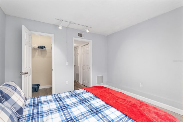 bedroom featuring a spacious closet, a closet, track lighting, and hardwood / wood-style flooring