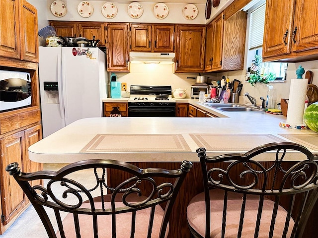 kitchen with kitchen peninsula, a kitchen bar, sink, and white appliances