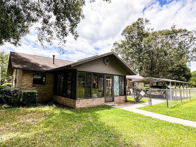 rear view of property featuring a sunroom, a lawn, and a carport