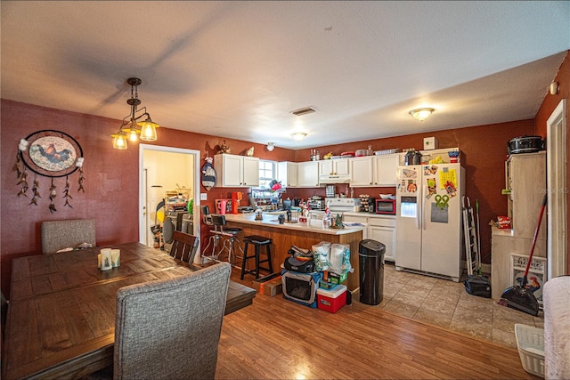 kitchen featuring white appliances, white cabinets, hanging light fixtures, kitchen peninsula, and a breakfast bar area