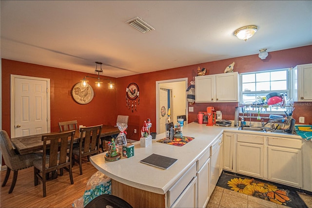 kitchen with kitchen peninsula, white cabinetry, sink, and pendant lighting