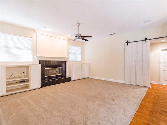 unfurnished living room featuring a fireplace, wood-type flooring, a barn door, and ceiling fan