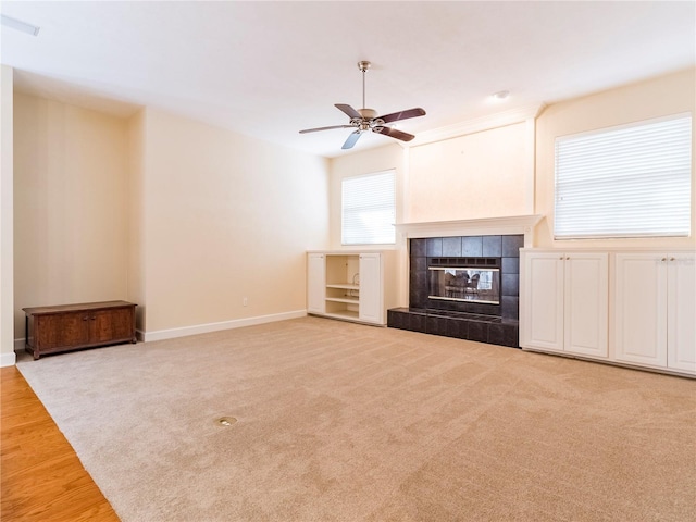 unfurnished living room with a tile fireplace, ceiling fan, and light carpet