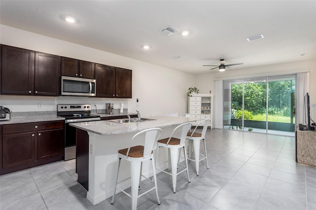 kitchen featuring a center island with sink, a kitchen breakfast bar, sink, ceiling fan, and stainless steel appliances