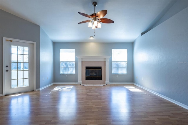 unfurnished living room with a tiled fireplace, ceiling fan, and wood-type flooring