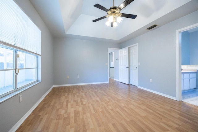 spare room featuring a tray ceiling, ceiling fan, and light hardwood / wood-style flooring