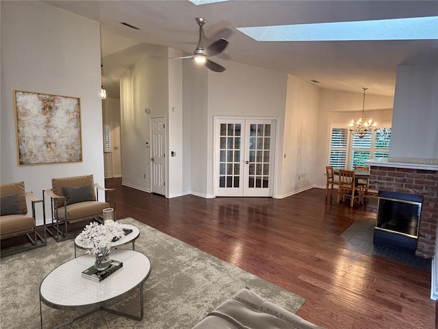 living room with french doors, a skylight, a brick fireplace, ceiling fan with notable chandelier, and dark wood-type flooring