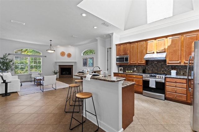 13554 NW 7th Rd, Newberry, FL 32669 - kitchen with stainless steel appliances, under cabinet range hood, light tile patterned floors, crown molding, and a kitchen bar