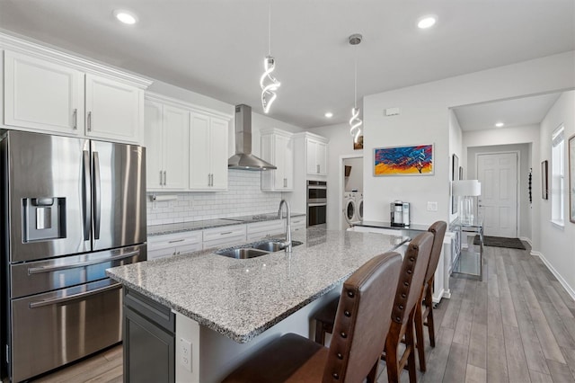 kitchen featuring stainless steel appliances, light stone counters, wall chimney exhaust hood, and sink