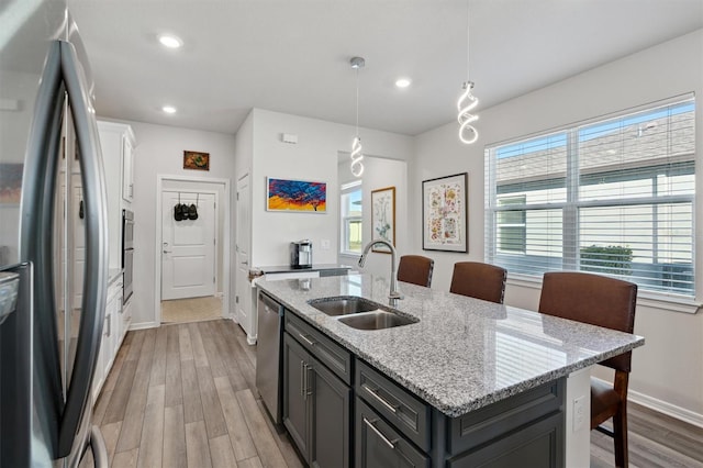 kitchen featuring light stone countertops, sink, an island with sink, decorative light fixtures, and appliances with stainless steel finishes